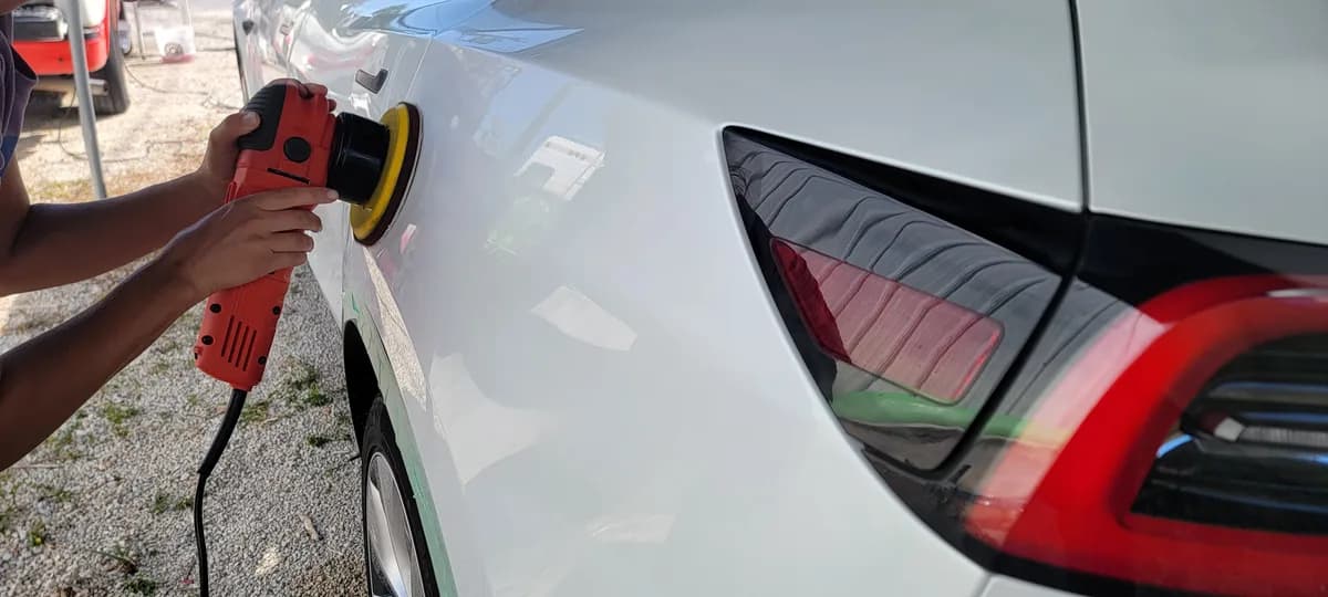 Machine-polishing a white car with an orbital buffer for a swirl-free finish